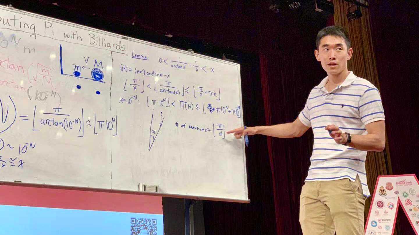 A man stands on stage in front of a whiteboard covered with equations and diagrams.
